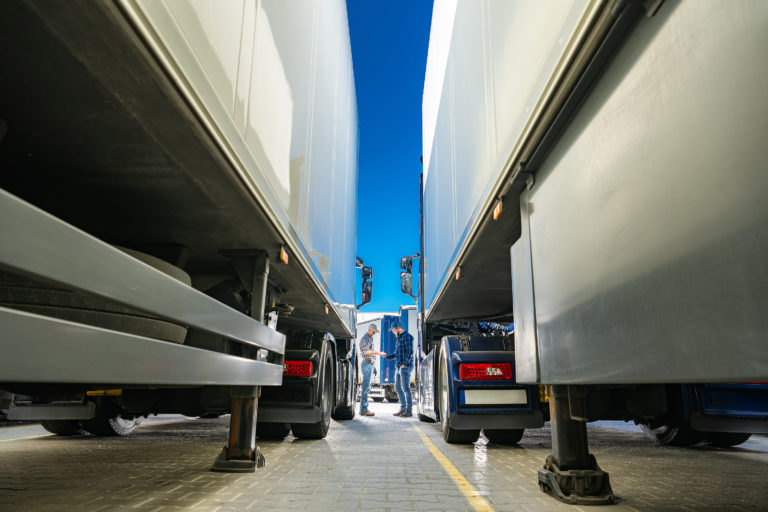 A fleet of trucks parked in an open lot and two caucasian drivers meeting